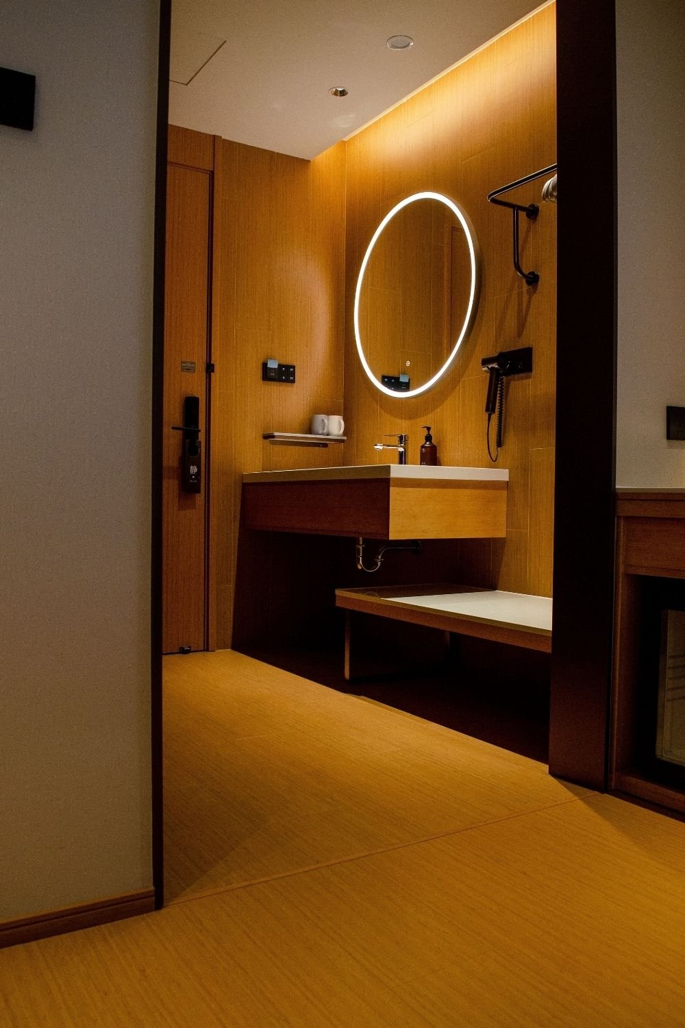 Hotel-style bathroom with wood-look walls, round backlit mirror and a floating wood vanity