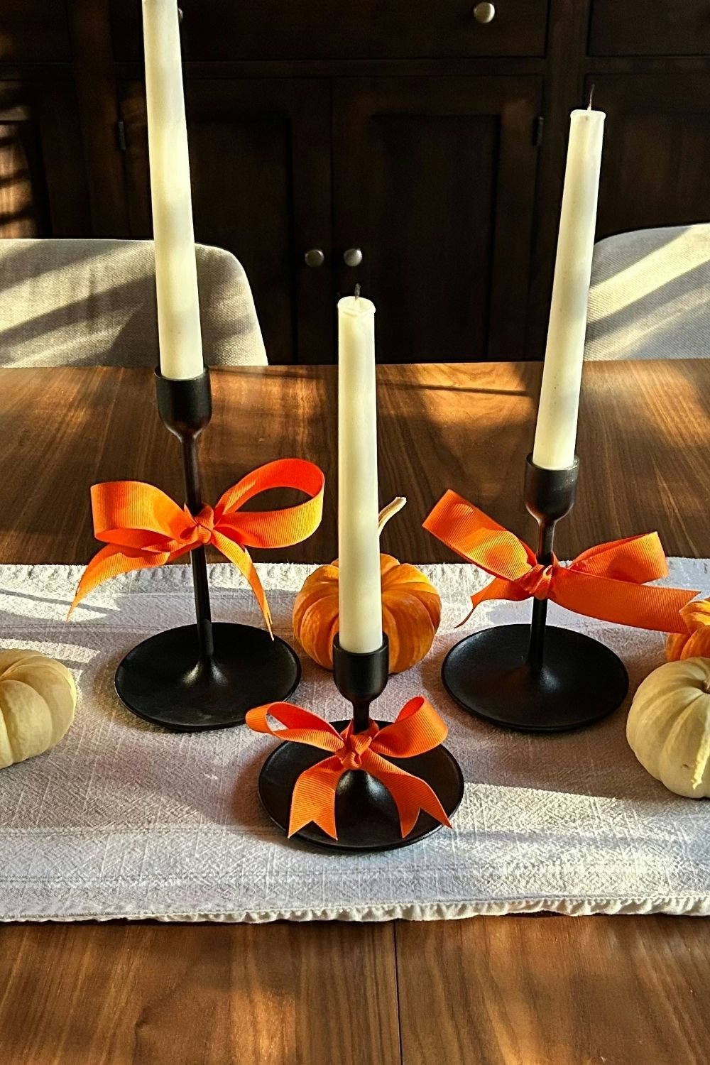 Black candlesticks tied with orange ribbon bows, ivory taper candles and mini pumpkins on a linen table runner