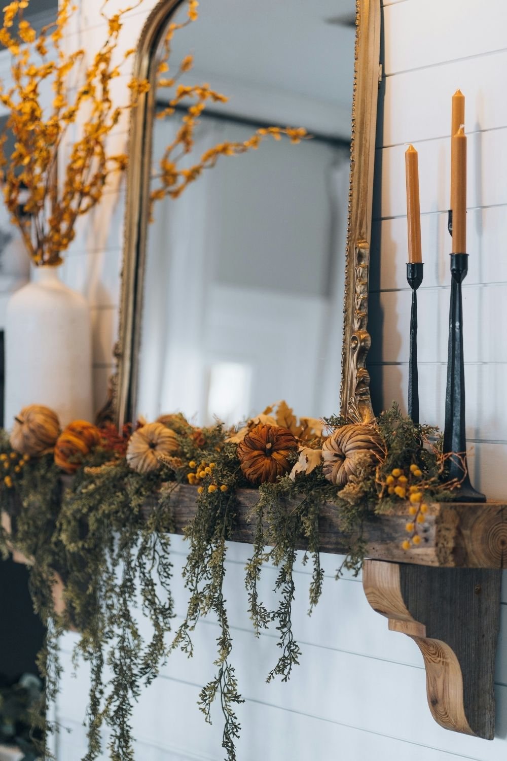 Rustic fall mantel with a trailing green garland, woven pumpkins, mustard taper candles and a gilded mirror
