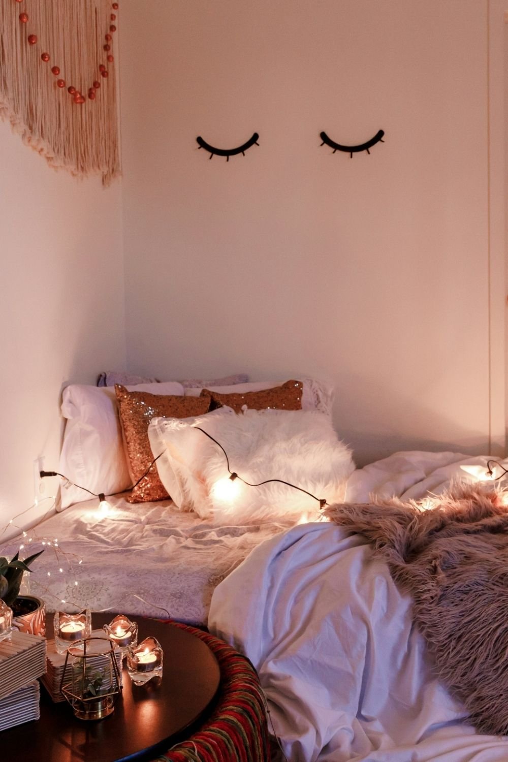 Boho bedroom corner with string lights, sequin and faux fur pillows, closed-eye wall decals, macrame and tealights