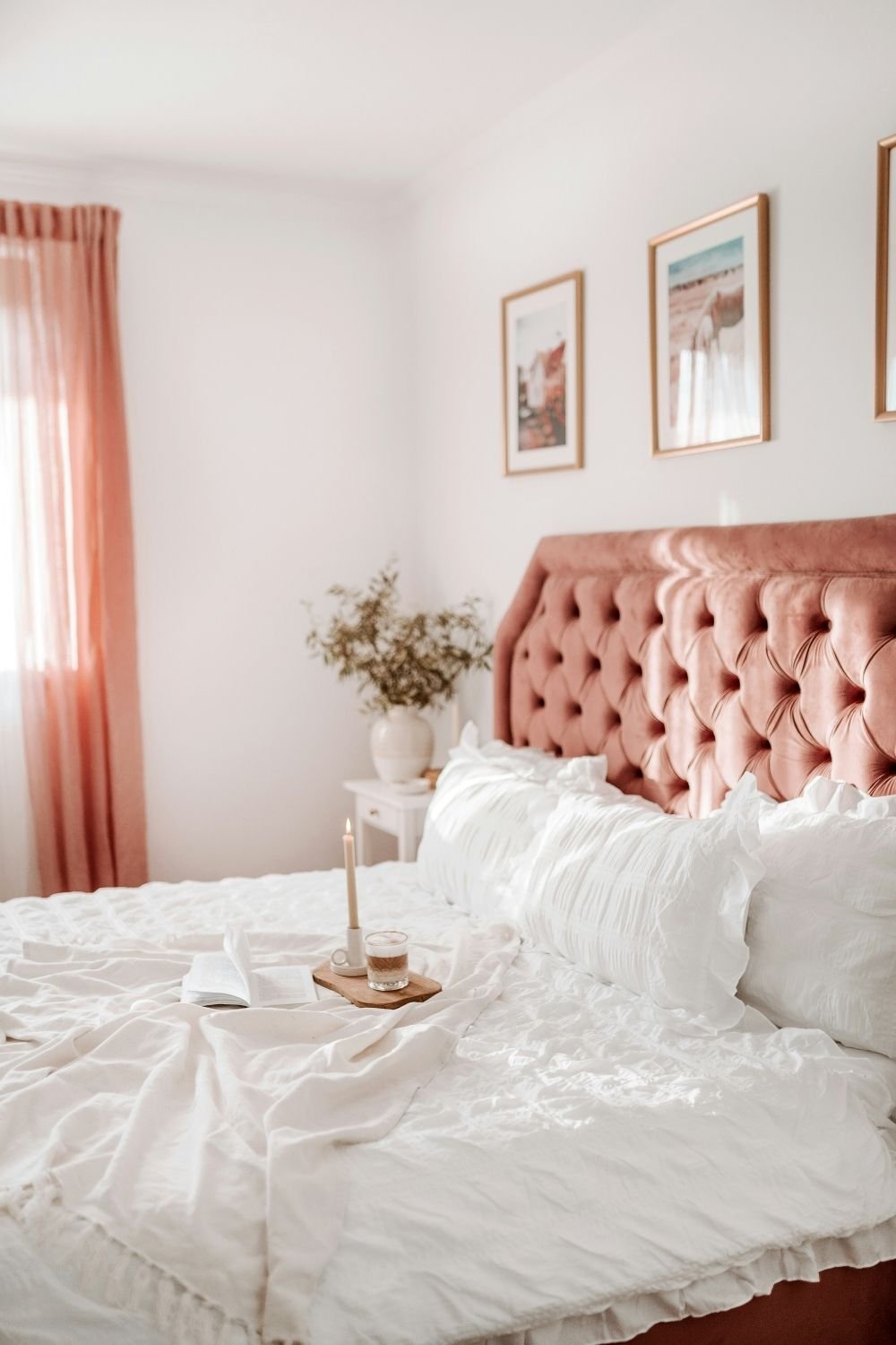 Dusty pink tufted velvet headboard with ruffled white bedding, pink linen curtains and gold framed prints