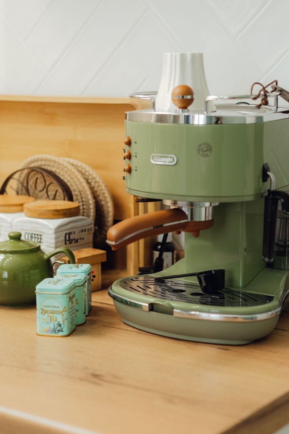 Sage green retro espresso machine on a wood counter with a green teapot, mint tea tins and a white coffee canister