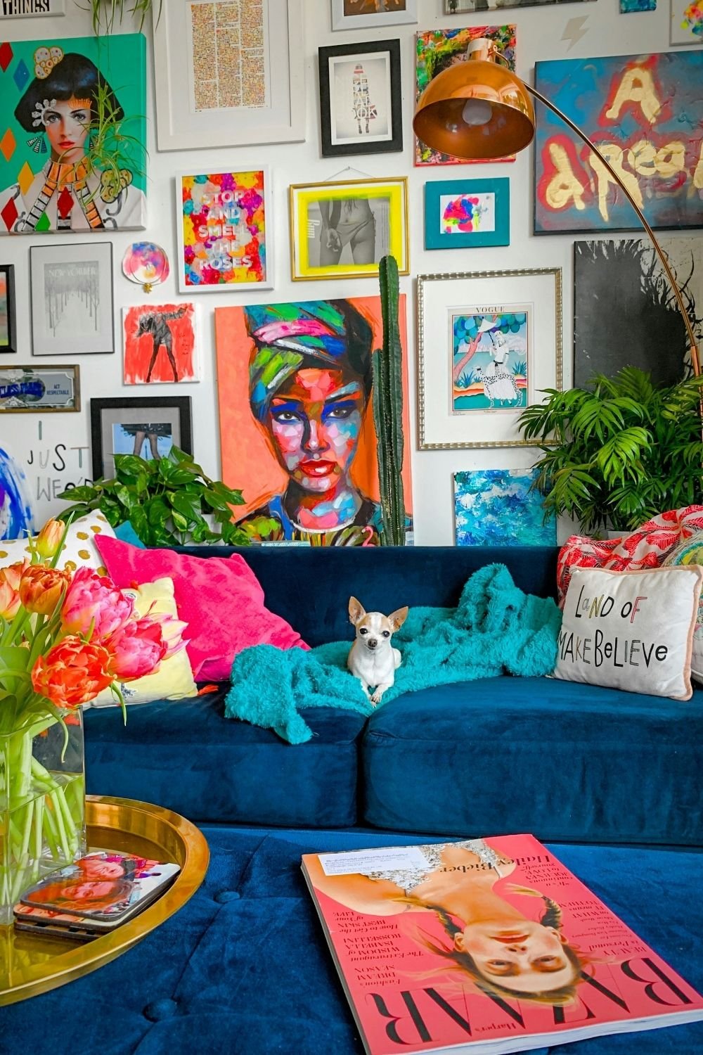 Colorful maximalist boho living room with a navy velvet sofa, a bright gallery wall, a copper arc lamp, plants and tulips