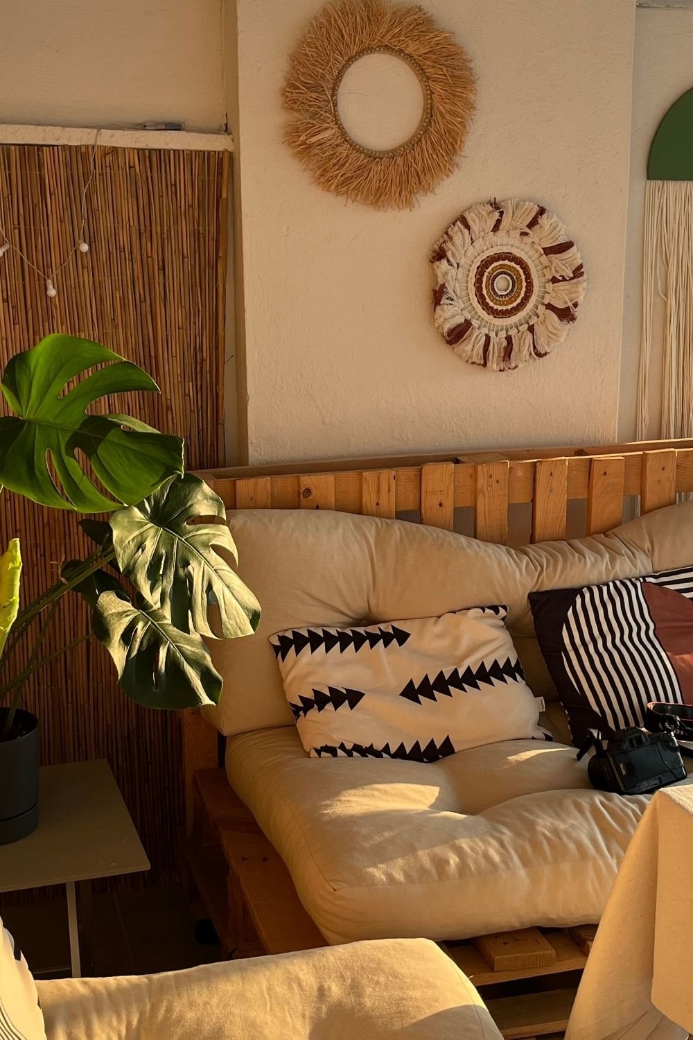 Boho pallet sofa with cream cushions, black and white patterned pillows, a raffia sun mirror and a woven wall hanging