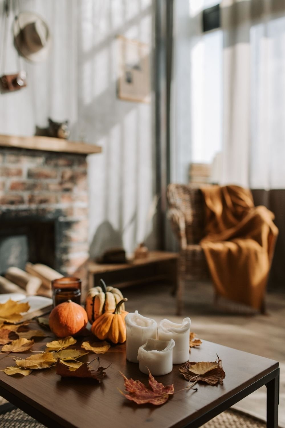 Coffee table with small pumpkins, white pillar candles and dried autumn leaves in a living room with a brick fireplace
