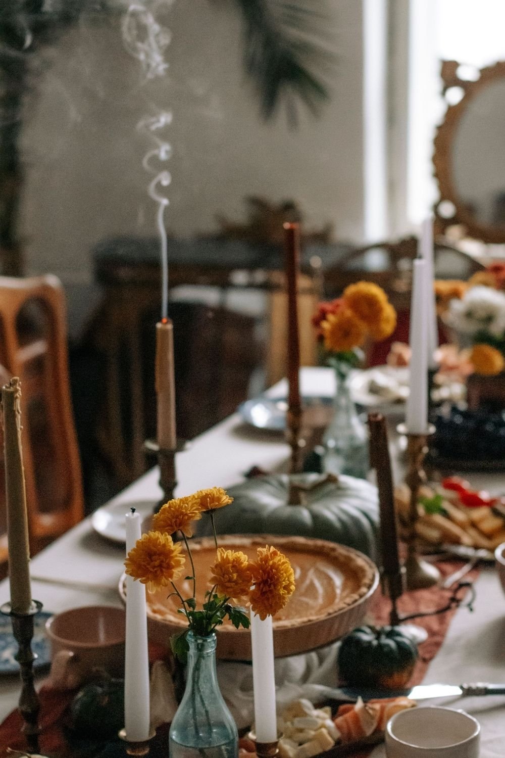Vintage Thanksgiving table with taper candles in brass holders, orange chrysanthemums, a green pumpkin and a pumpkin pie
