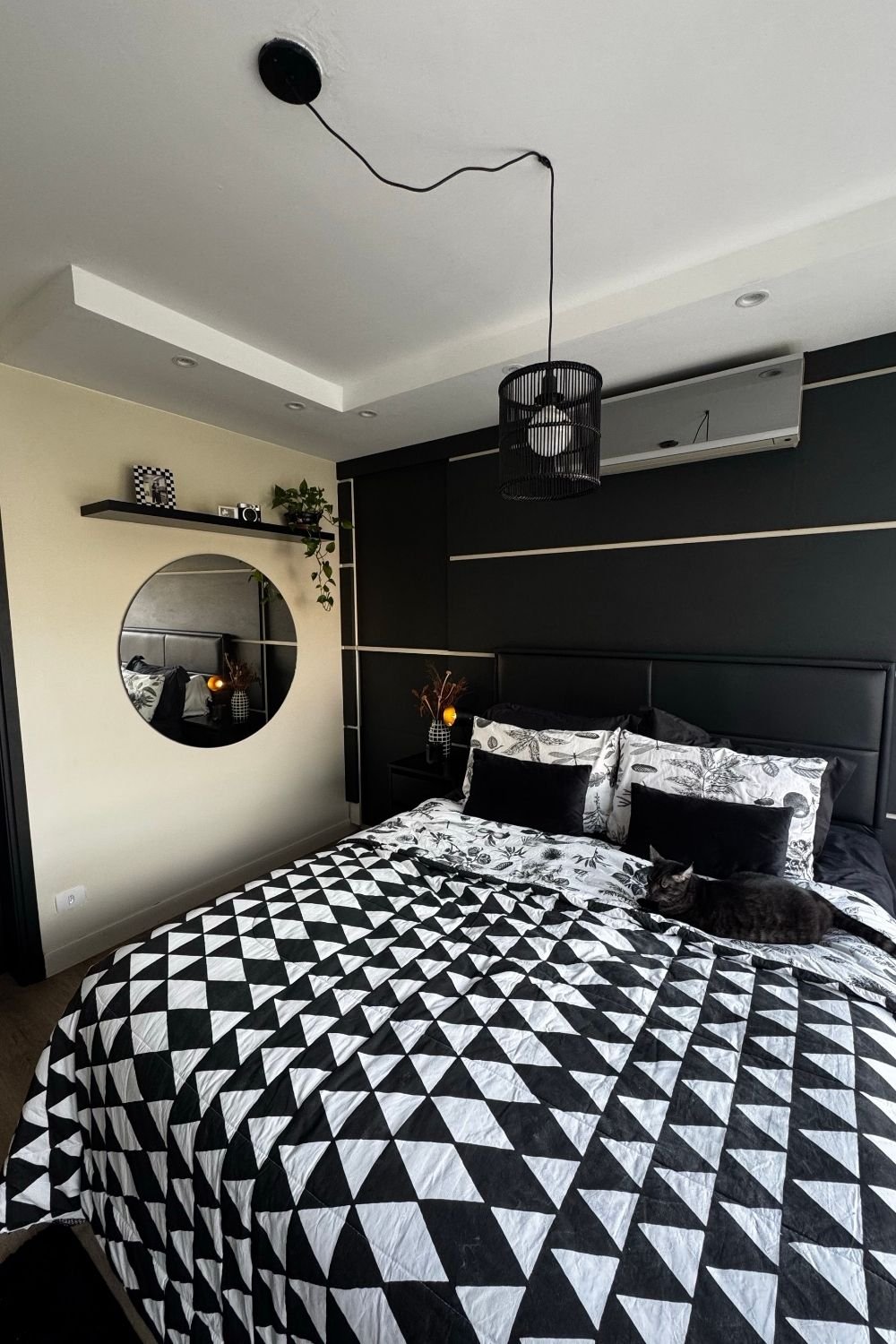 Bedroom with a black feature wall with beige inlay strips, black headboard and black-and-white geometric quilt