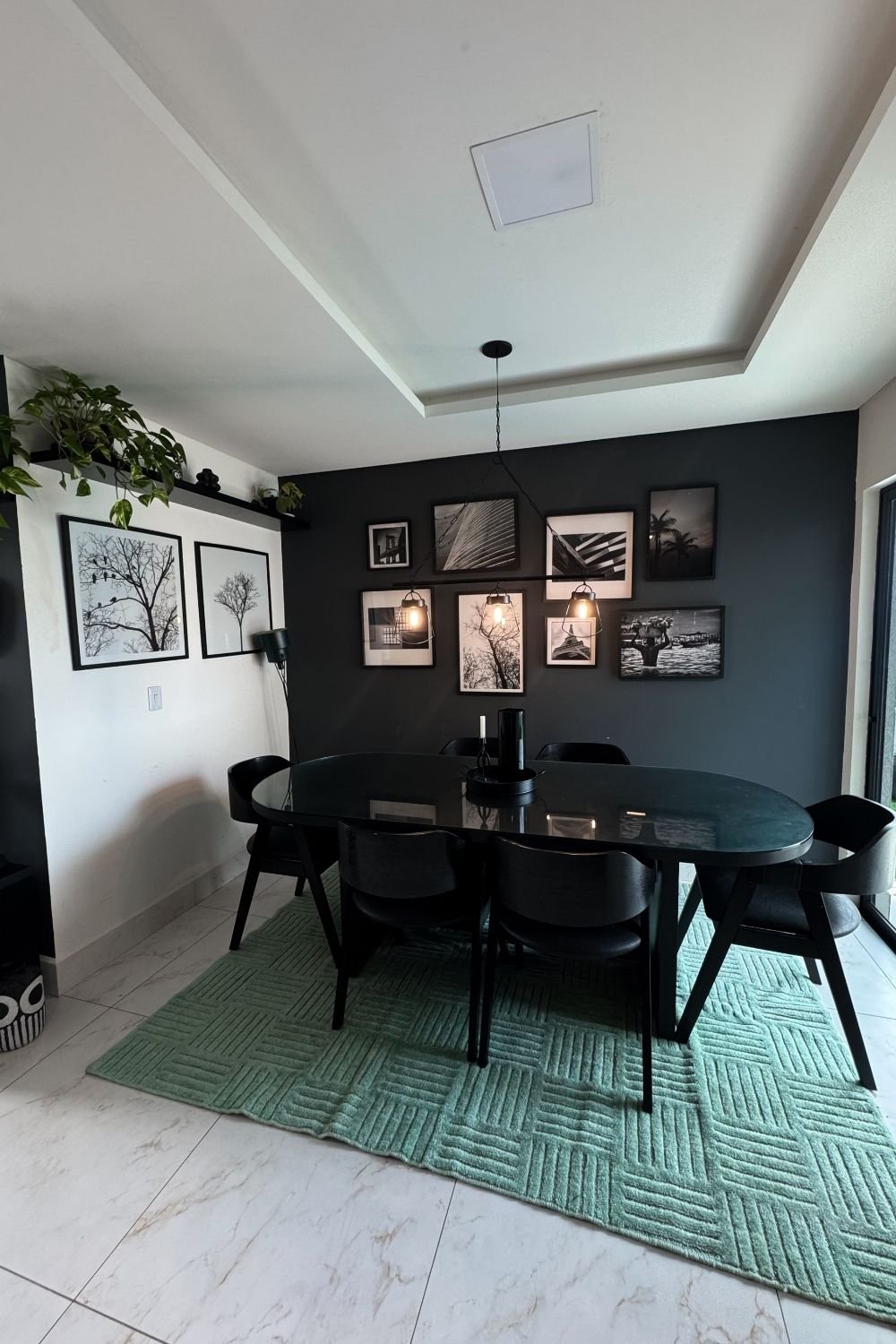 Dining area with a charcoal gallery wall of black-and-white photos above an oval black table and a green rug