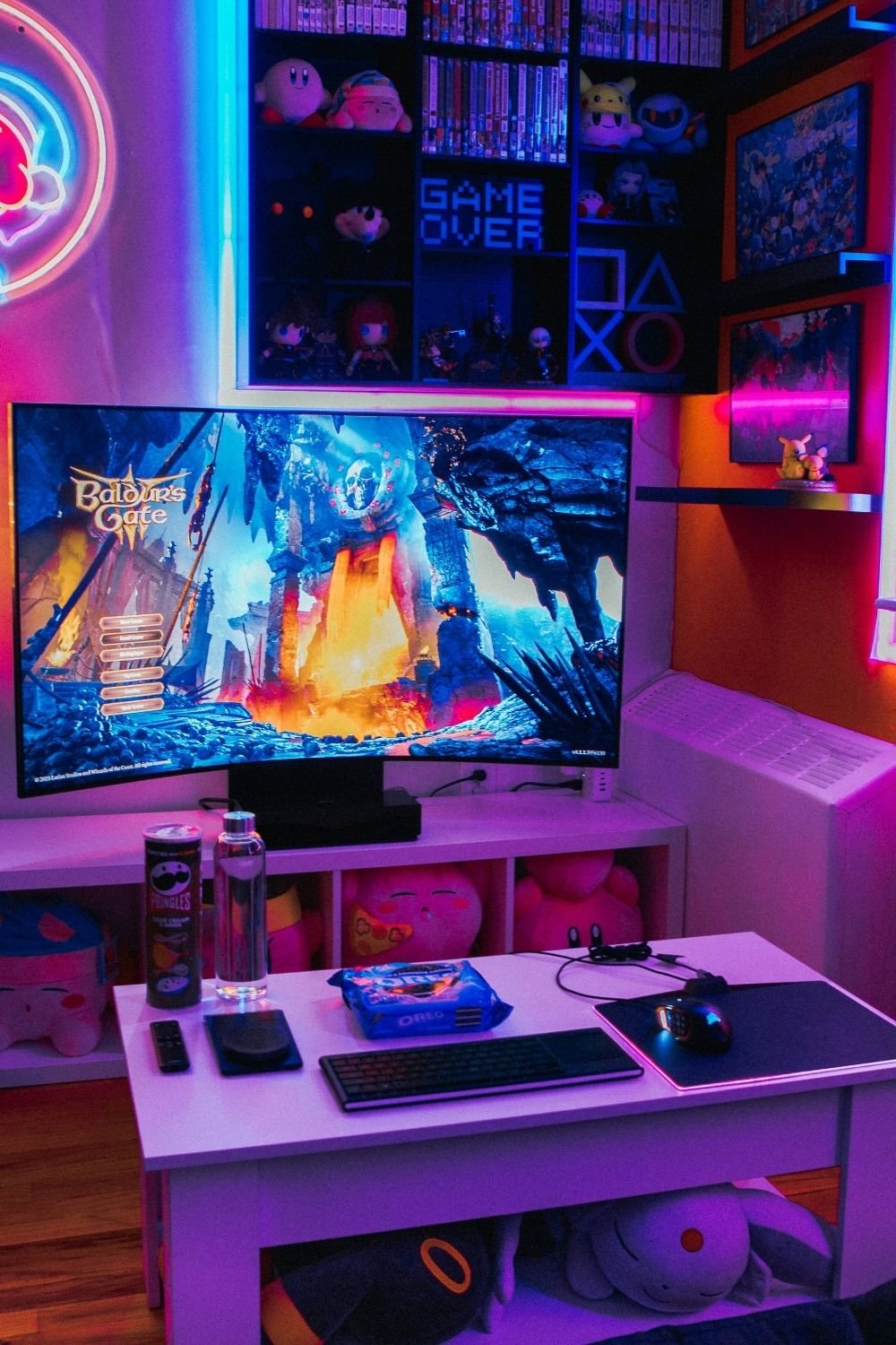 Colorful gamer room with a curved monitor on a cube unit, a low white table with keyboard and mouse, and a neon-lit display cabinet