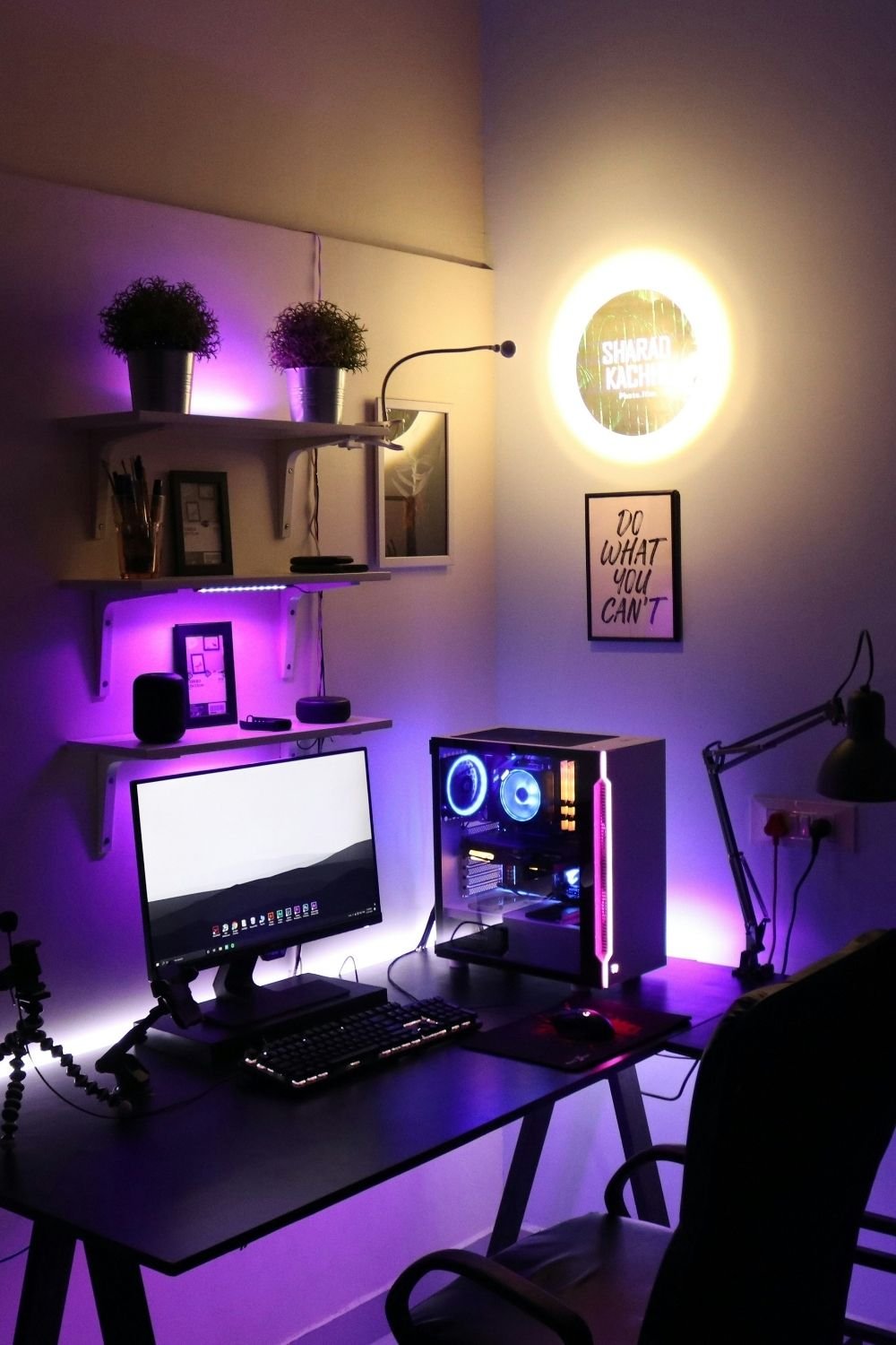 PC gaming setup with purple RGB lighting, a glass-sided PC case, floating shelves with plants and a backlit wall sign
