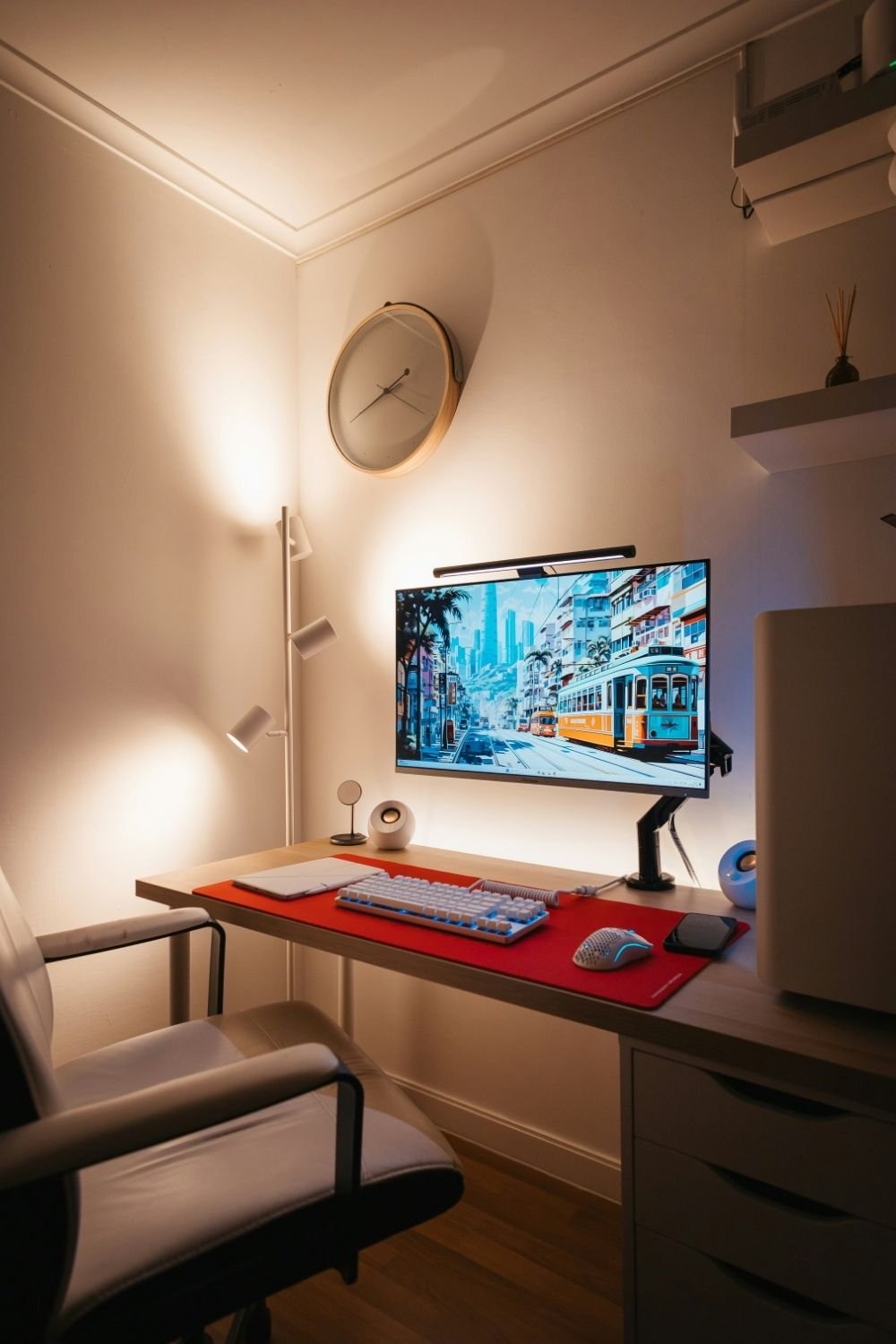 Small alcove gaming desk with a monitor arm, light bar, red desk mat, white keyboard and a floor lamp
