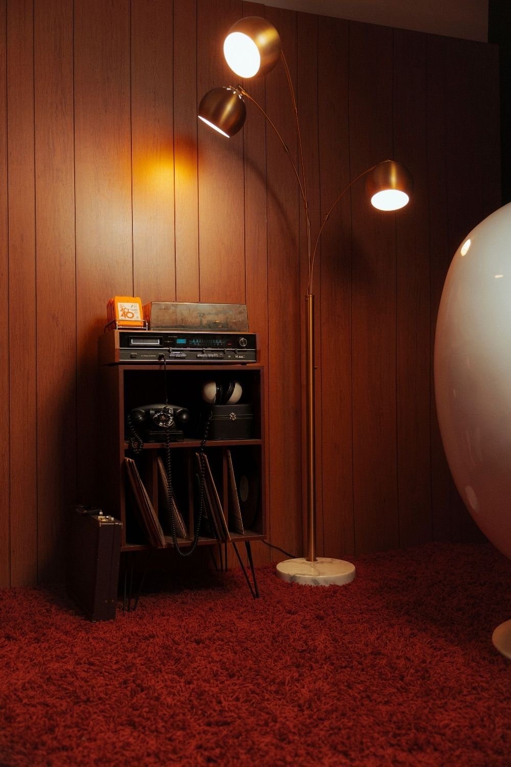 Retro corner with wood paneling, a record cabinet, vintage receiver, brass arc lamp and red shag carpet