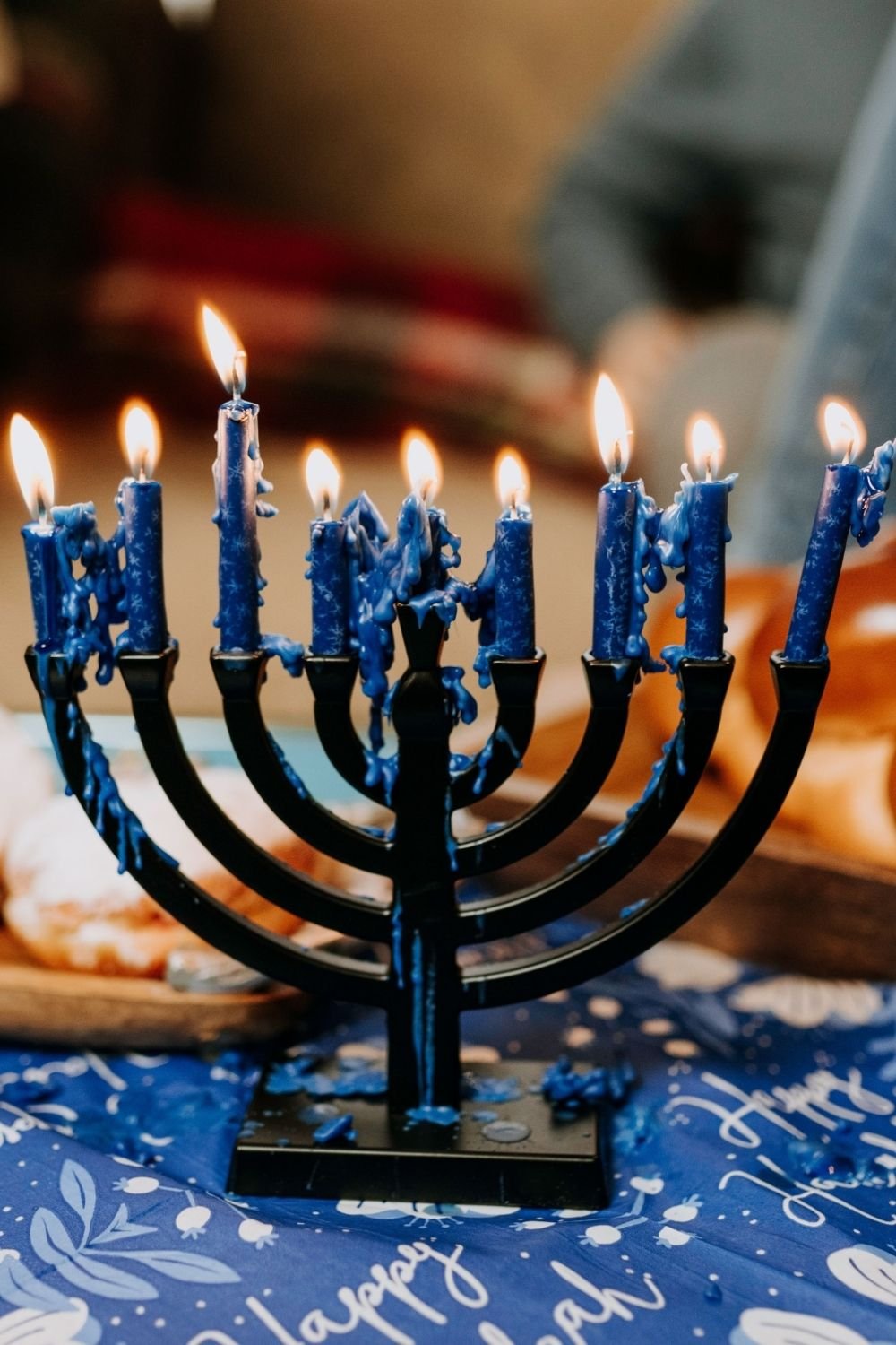 Black menorah with nine lit blue candles and dripping wax on a blue and white printed cloth