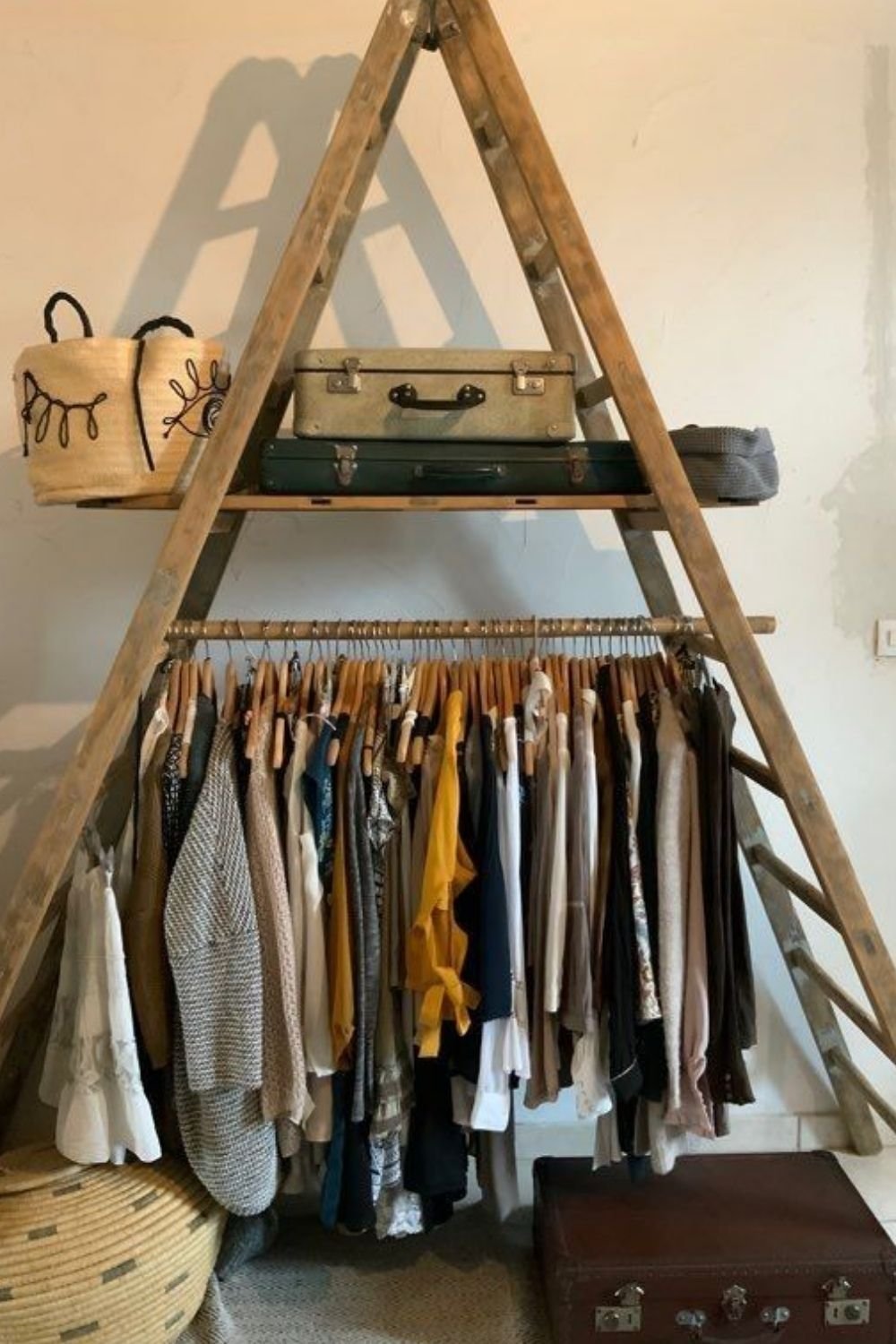 Step ladder used as a clothing rack with a bamboo pole across it and vintage suitcases on the top platform