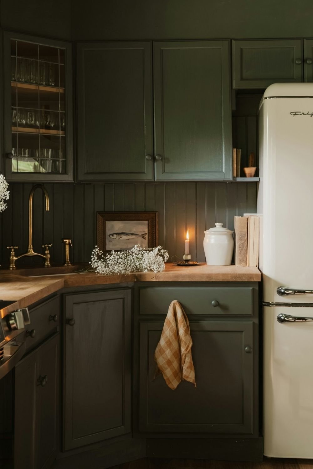 Dark green kitchen corner with leaded glass cabinet, brass tap, butcher block counter and a lit candle