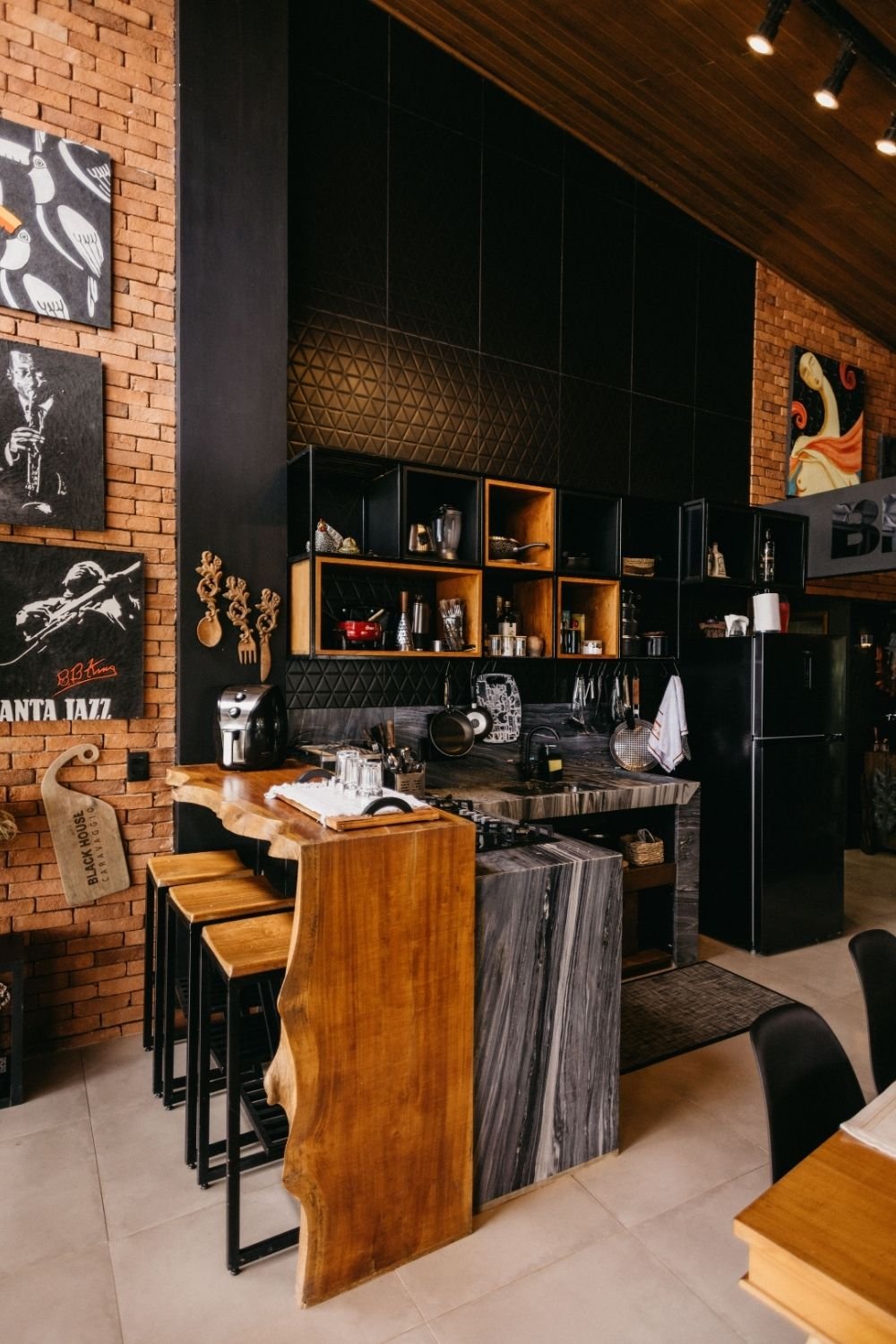 Dark urban kitchen with black tiles, exposed brick, black box shelving and a live-edge wood bar top