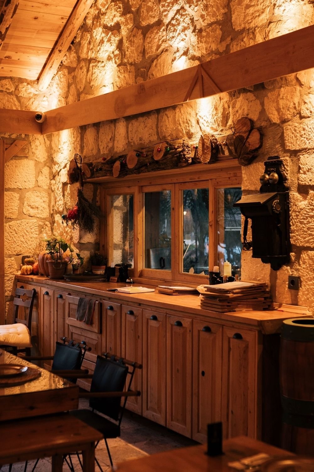 Rustic kitchen with a lit limestone wall, pine cabinets, thick wood counter and drying herbs
