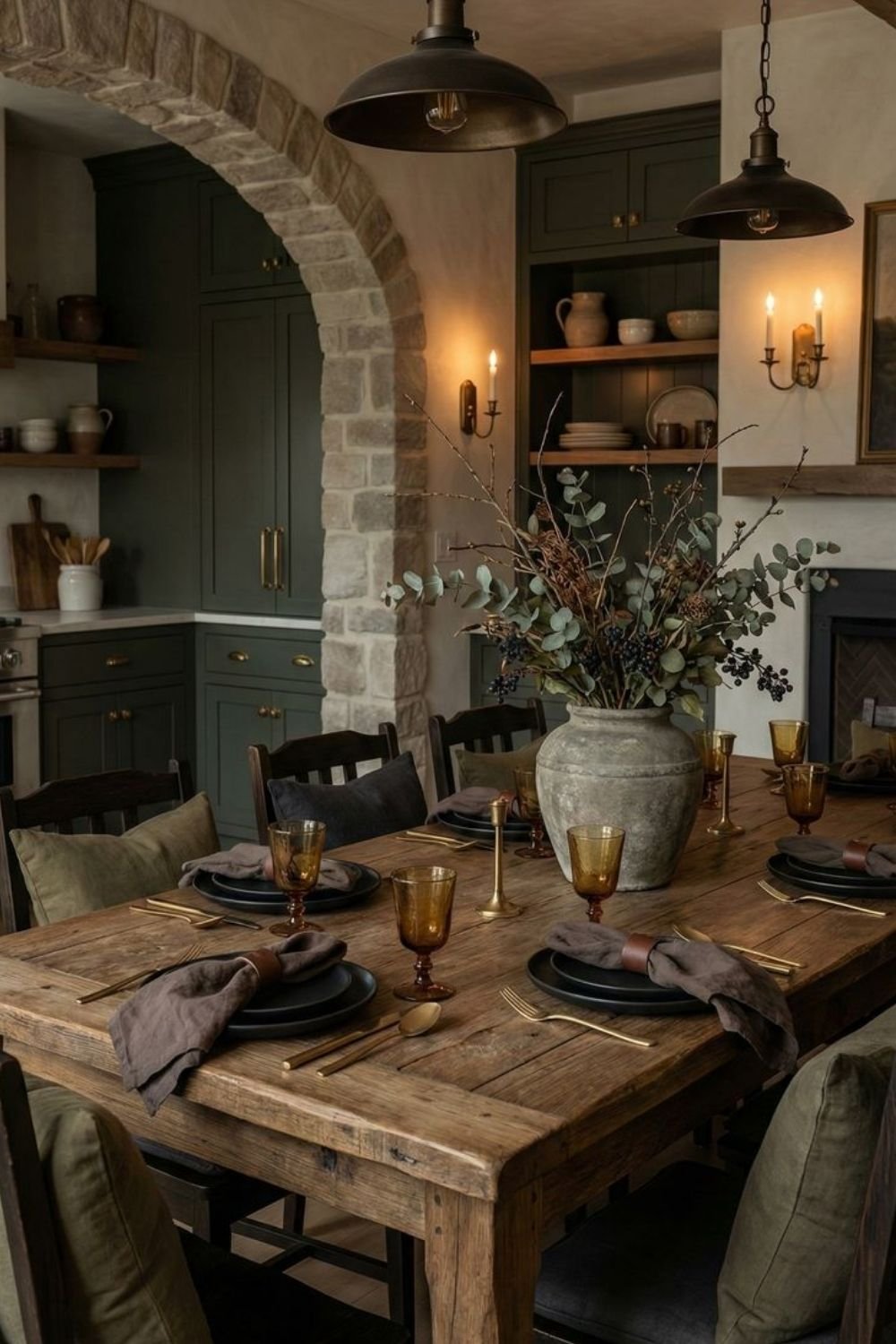 Dining table under a stone arch with black plates, brass cutlery, amber glasses and a stone urn of eucalyptus