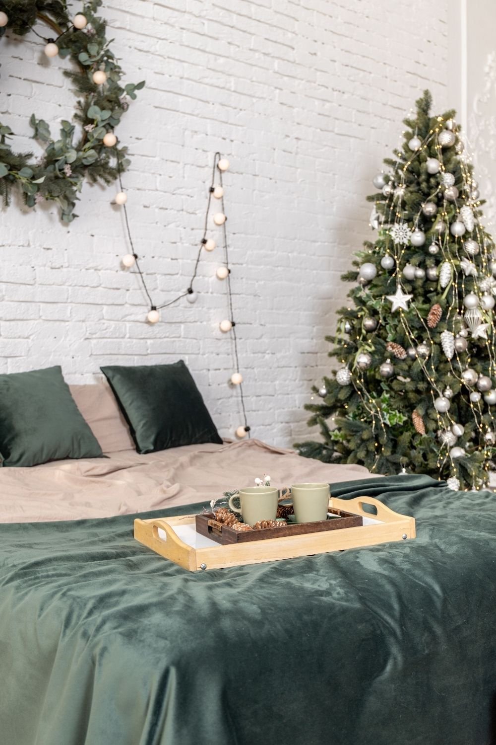 Christmas bedroom with a green velvet throw, eucalyptus wreath, bulb lights and a tray with green mugs