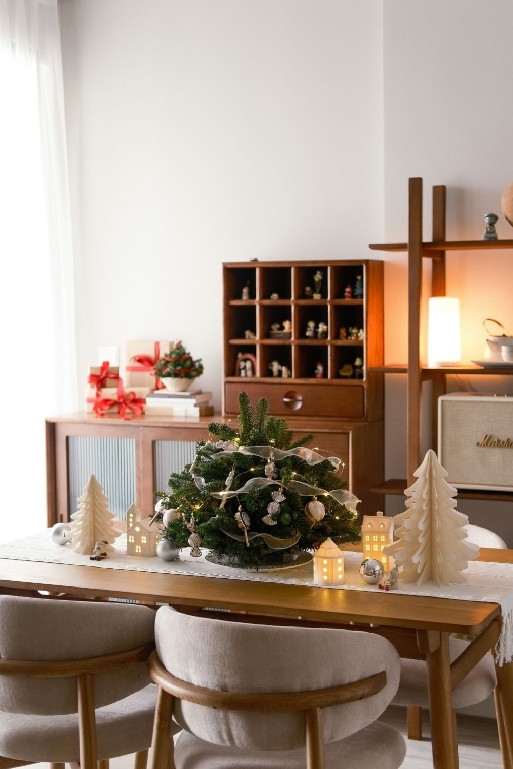 Dining table with a small fir centerpiece with fairy lights, paper trees and lit ceramic houses