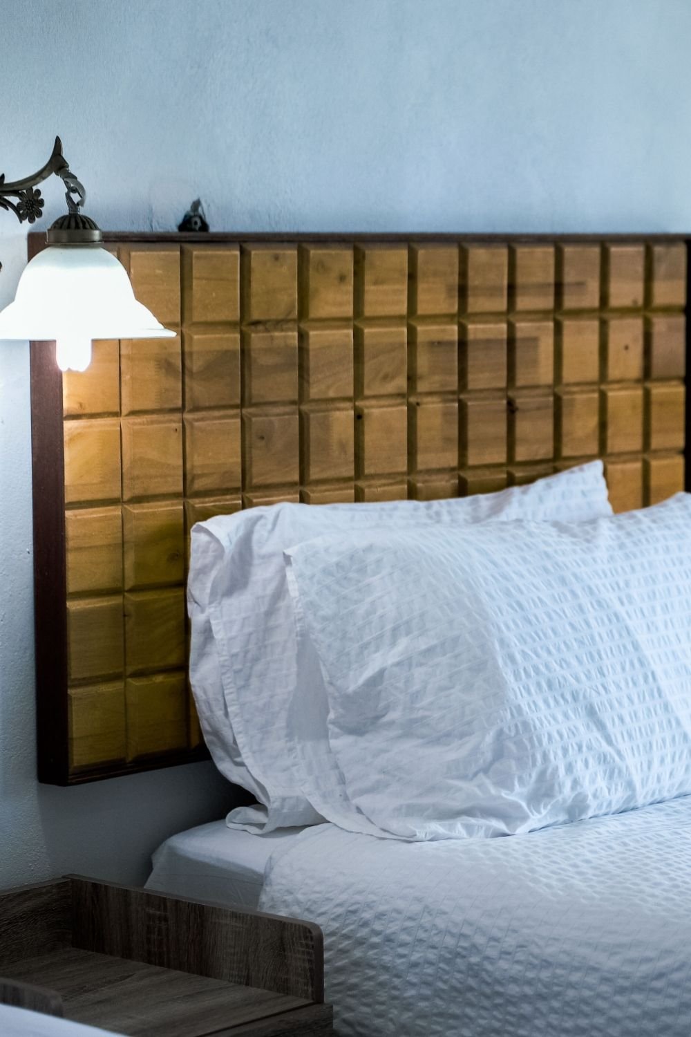 Wooden headboard with a grid of carved squares on a pale blue wall, lit by a brass sconce