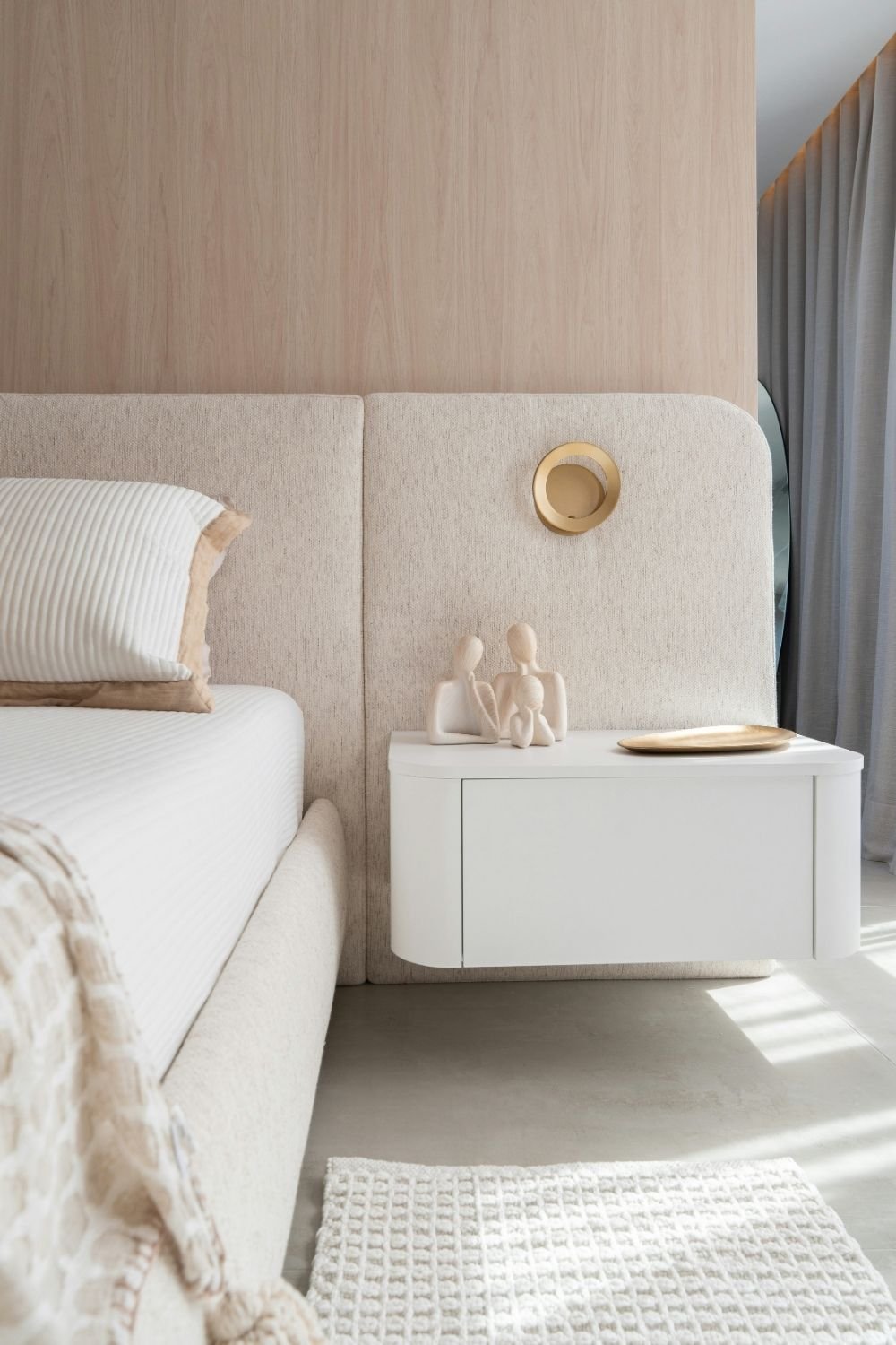 Bedroom with a pale oak panel wall, rounded oatmeal upholstered headboard and a white floating nightstand