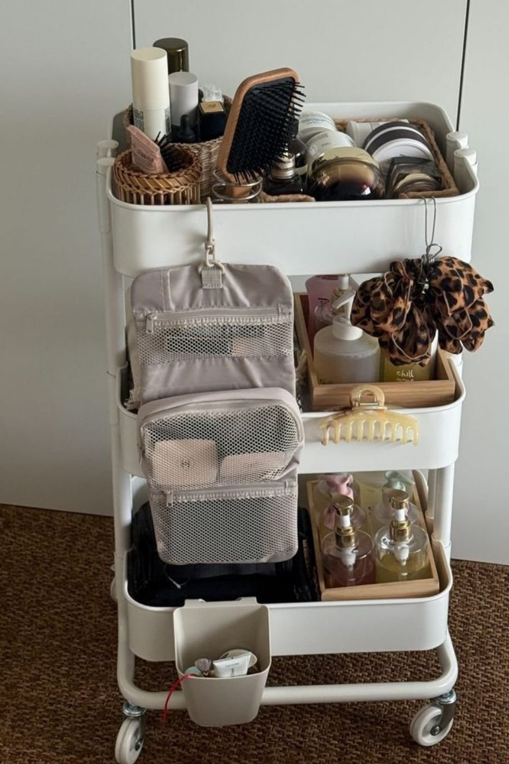 Three-tier white rolling cart set up as a dorm bathroom cart with toiletries, towels and a hanging wash bag