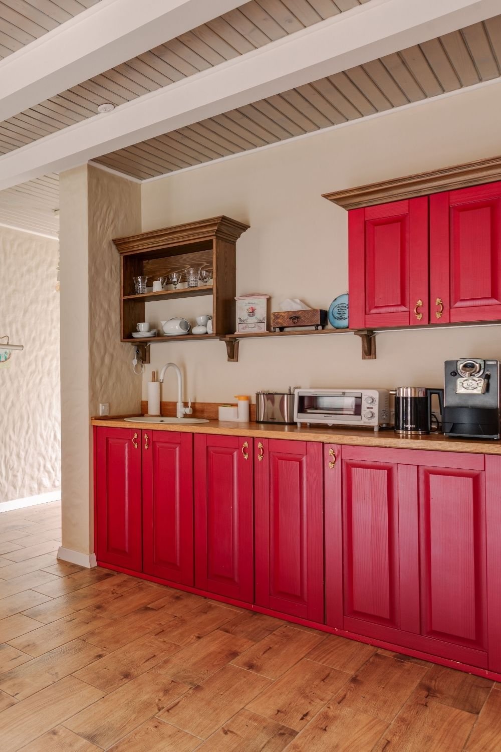Country kitchen with raspberry red panelled cabinets, brass handles, wood worktop and cream plaster walls