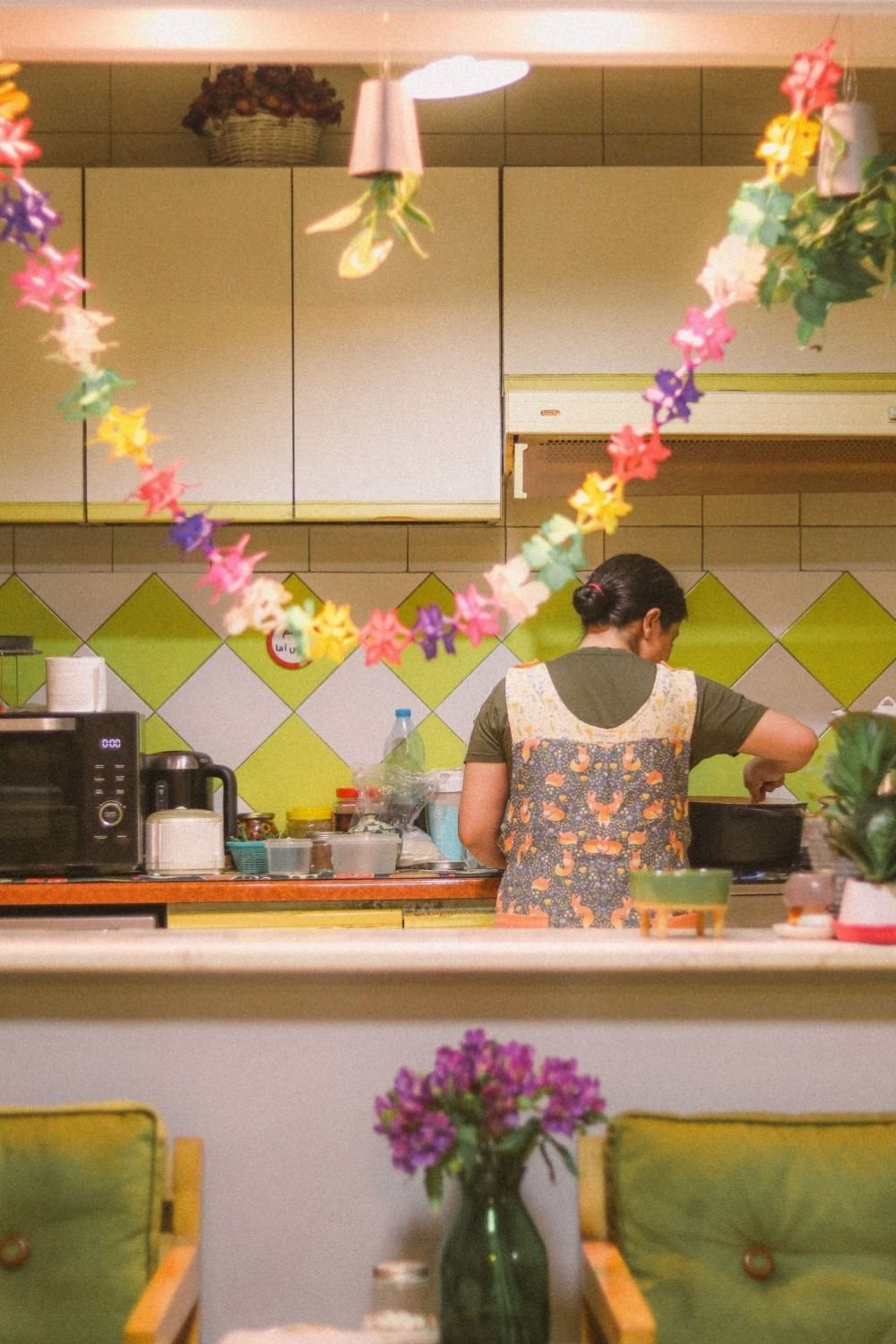 Kitchen with a lime and white diamond tile backsplash, cream cabinets and a paper flower garland