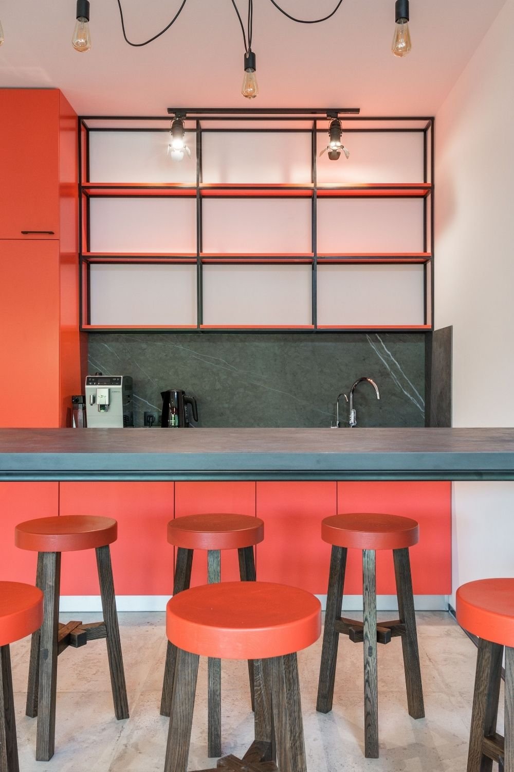 Coral kitchen with dark green marble backsplash, black metal shelving and coral-topped bar stools