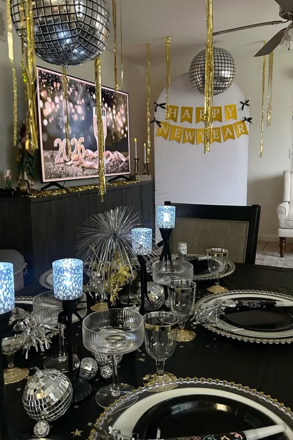 Black and gold New Year's Eve table setting with beaded chargers, party horns, a silver firework centerpiece and gold ceiling streamers