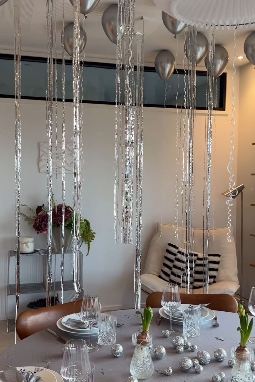 Silver New Year's Eve table with chrome balloons on the ceiling, hanging tinsel tails, crystal glasses and hyacinth bulbs in vases
