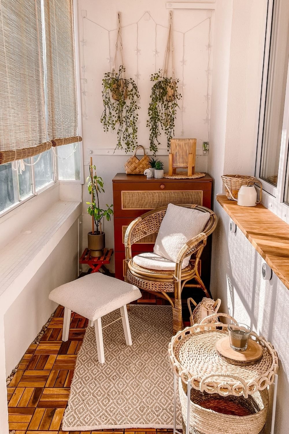 Enclosed rental balcony with wood deck tiles, a jute rug, a rattan armchair, hanging trailing plants and bamboo blinds