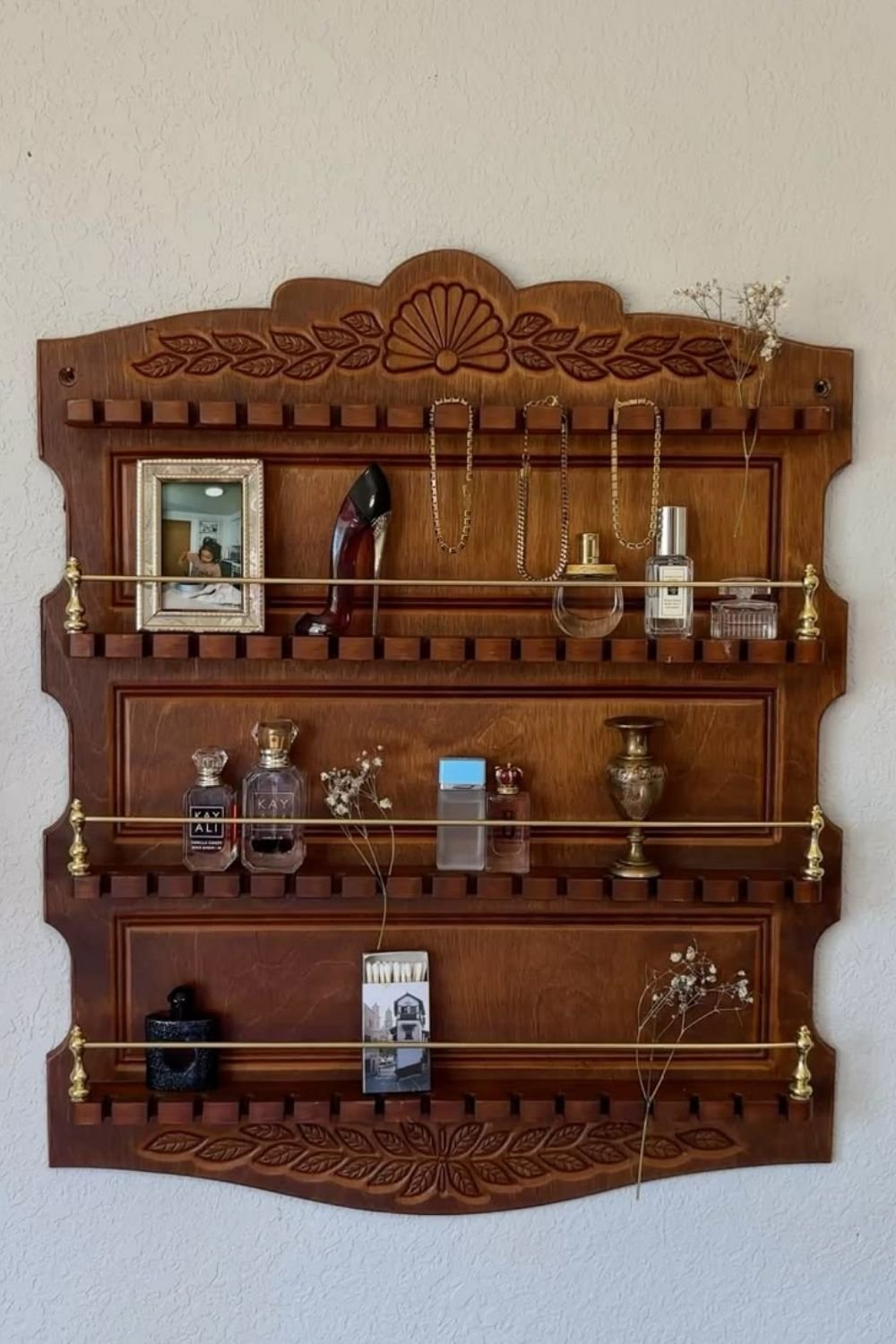 Carved vintage wooden plate rack reused as a display for perfume bottles, hung necklaces and dried flowers