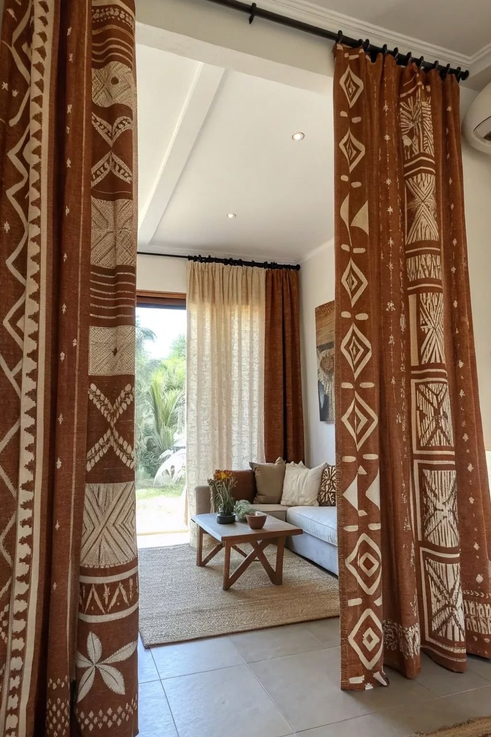 Living room seen through rust and cream mudcloth pattern curtains, with a plain gray sofa and jute rug beyond