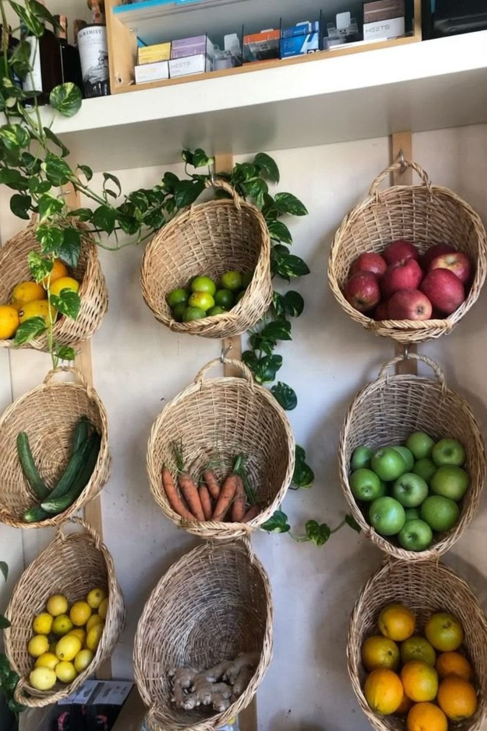 Nine wall mounted wicker baskets holding fruit and vegetables on a kitchen wall, with a pothos trailing through them